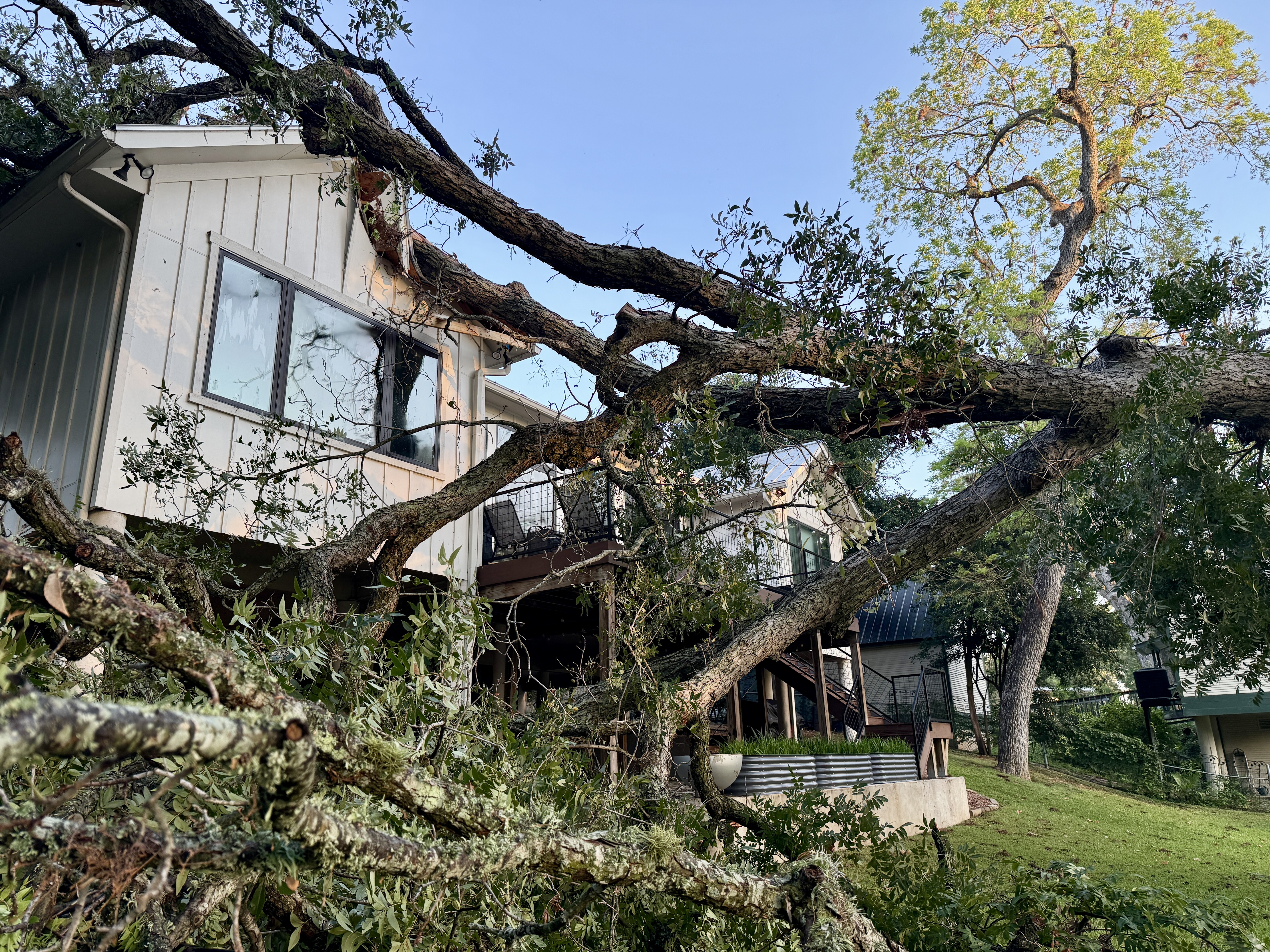 Multiple large tree limbs smashed into a two-story home and deck area.