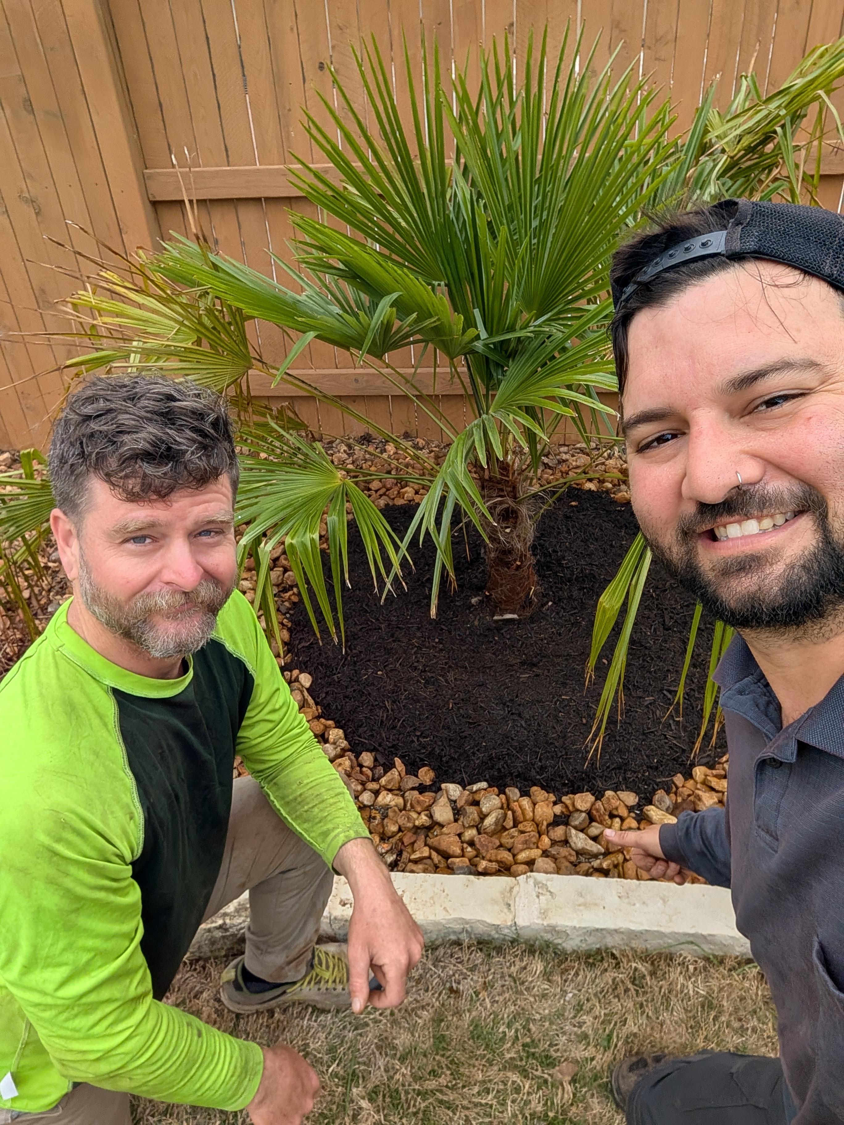 Kyle and Adam smiling next to a newly planted and mulched palm tree